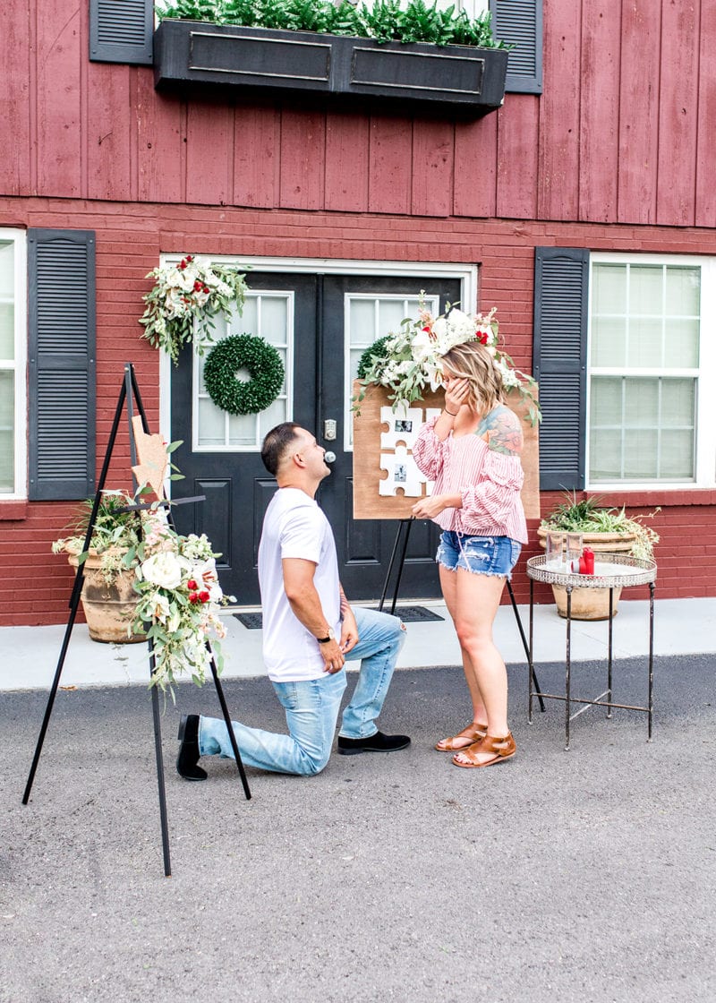 man proposing in front of red barn and flowers