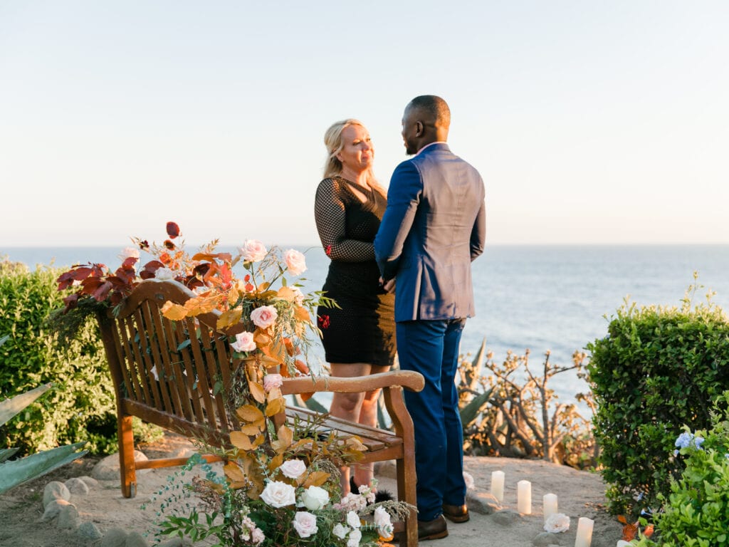 Couple standing at bench in front of ocean