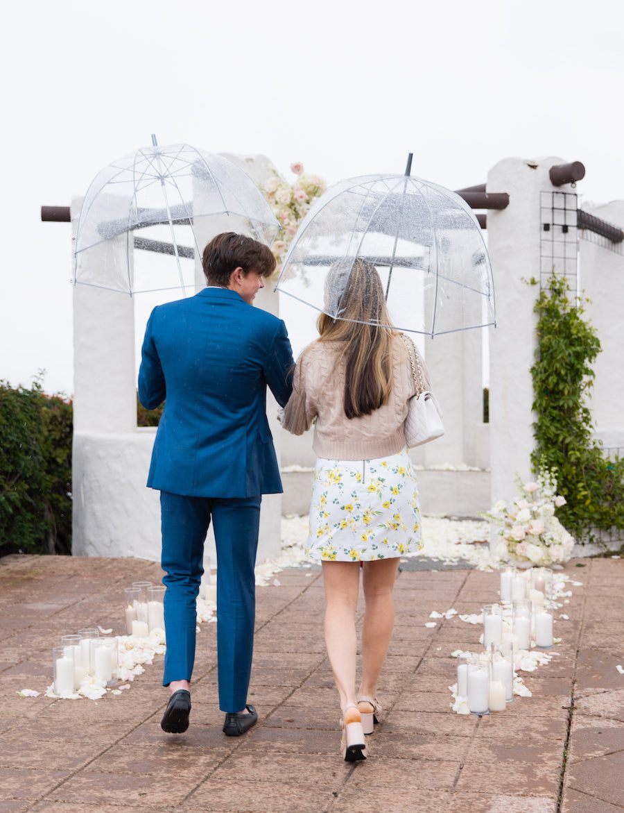 the couple walking to their magical rainy day proposal set up