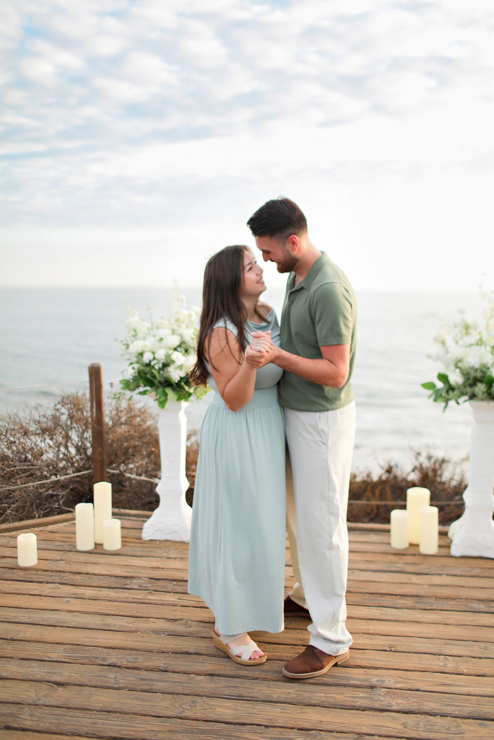 Couple holding hands on a wooden deck above the Pacific at a Crystal Cove proposal