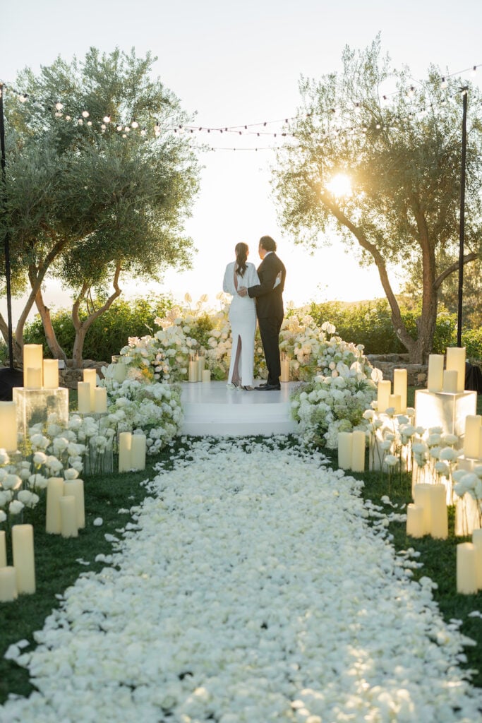 Luxury Malibu proposal scene with a floral-lined aisle and white ceremony platform at sunset