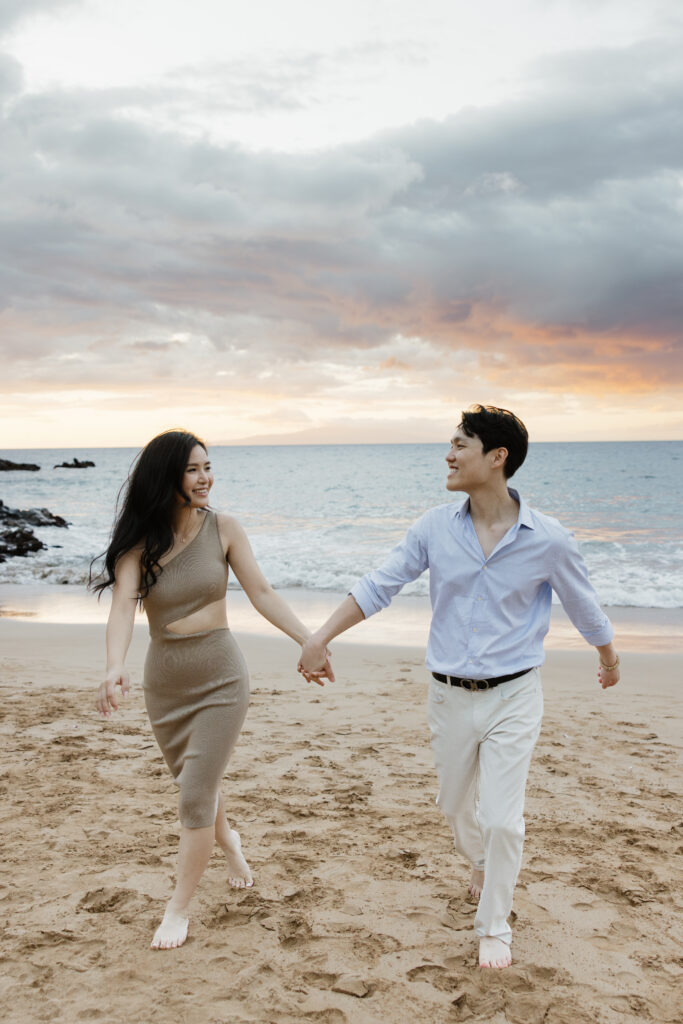 Couple walking hand in hand on a Maui beach at sunset after their Grand Wailea proposal