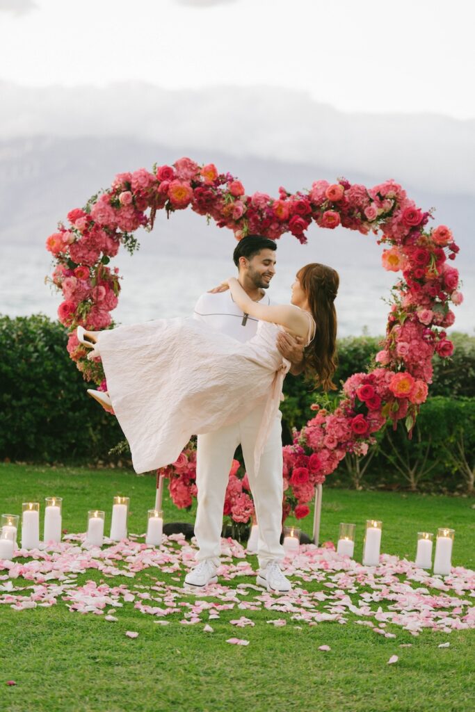 He lifts her under a pink rose heart arch at an Andaz Maui proposal