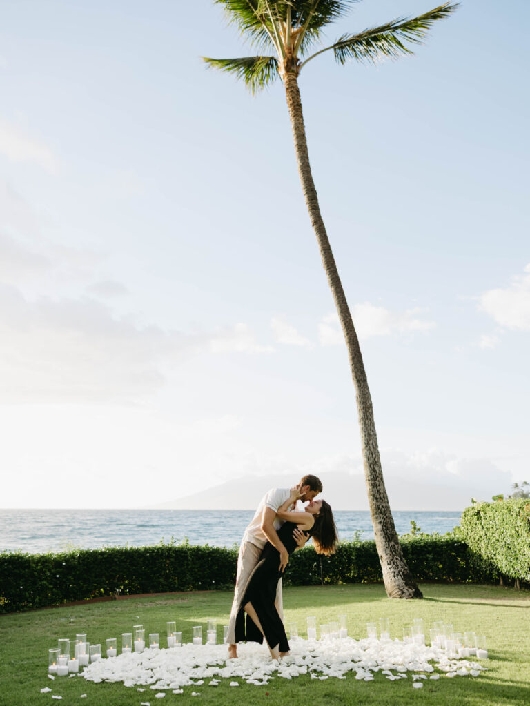 Couple kissing under a palm tree beside a white petal ring at the Grand Wailea