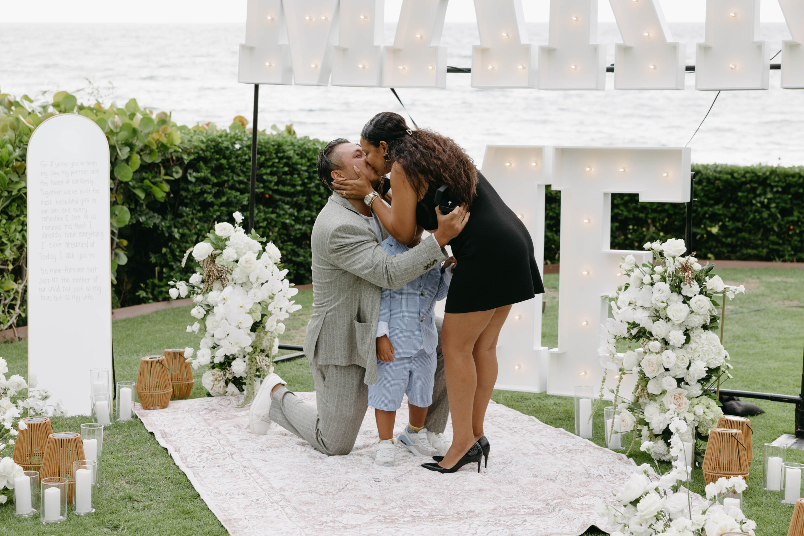 Couple embracing at a white floral proposal setup with a white arbor at the Grand Wailea