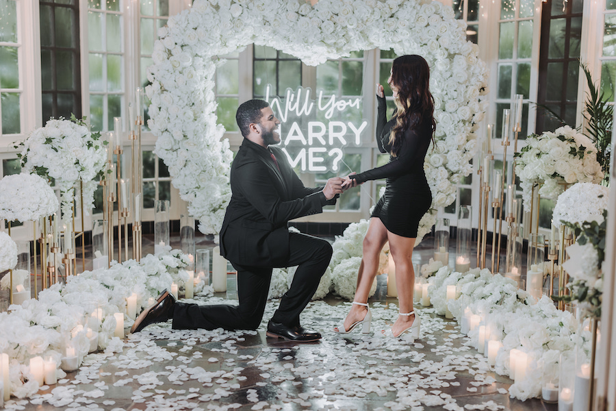 Proposal at a floral arch with candles, featuring Derrick proposing to Vanesa.