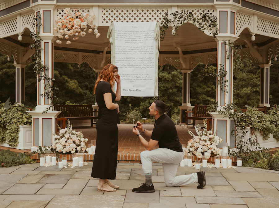 Romantic wedding proposal at a gazebo with flowers, featuring TJ proposing to Lindsey outdoors.