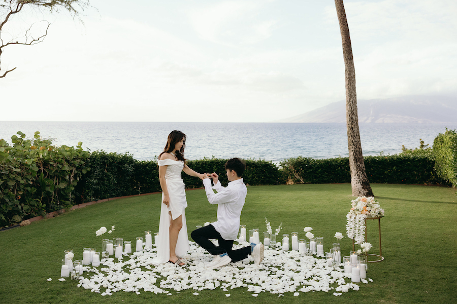 Romantic beach wedding proposal with couple, candles, and ocean view.