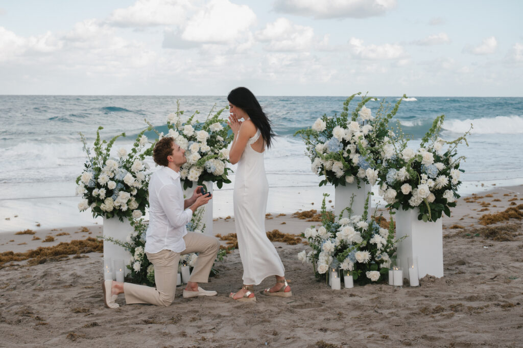 Proposal on the beach with floral arrangements and ocean backdrop.
