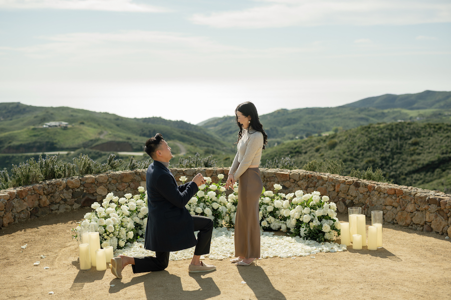Malibu engagement proposal with couple, scenic ocean view, romantic setting, and floral decor.