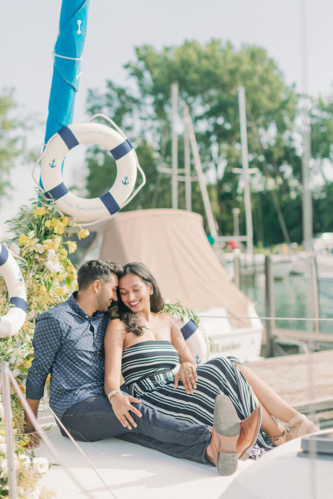 Romantic couple sitting by the marina, enjoying a sunny day with sailboats and nautical decorations.