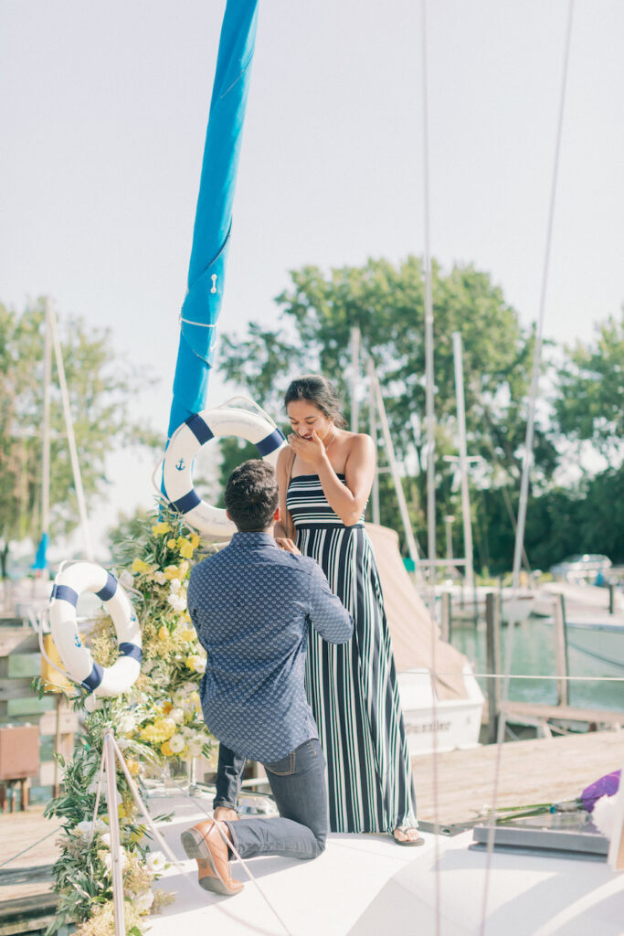 Romantic proposal scene featuring a man kneeling with a woman on a boat dock, surrounded by nautical.
