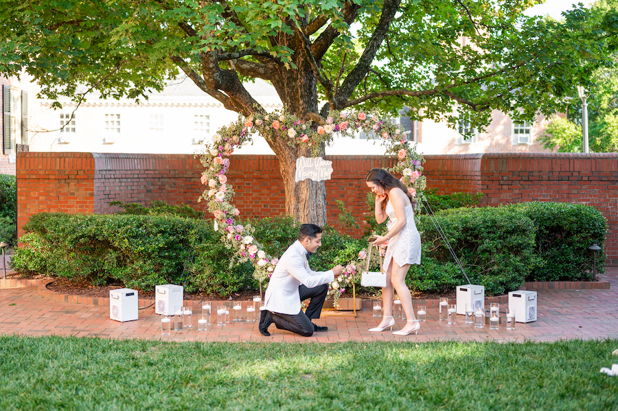 Romantic outdoor proposal under a heart-shaped floral arch with a couple.