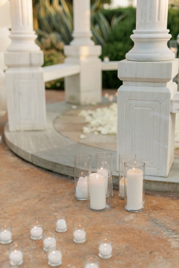 Pillar candles and white rose petals inside a white gazebo for a romantic proposal