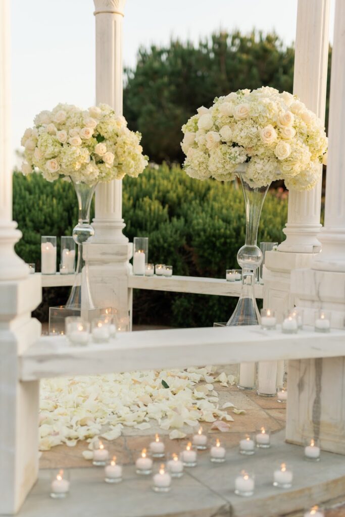 White rose arrangements and candles on gazebo benches for an all-white proposal
