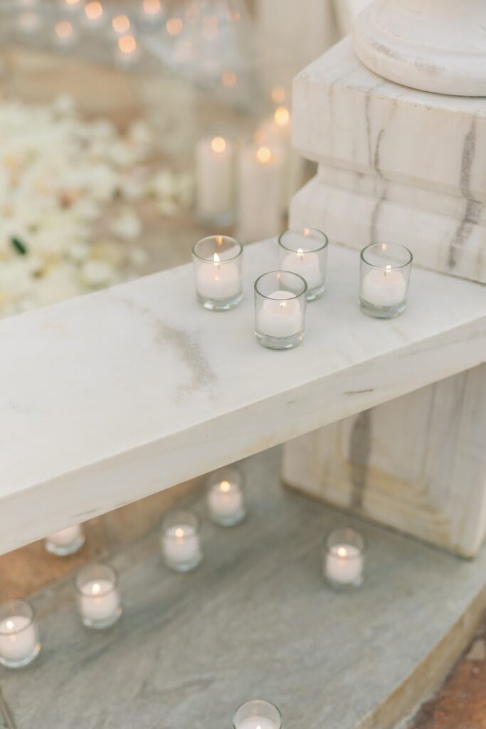 Glass votive candles on a marble gazebo bench at an all-white proposal