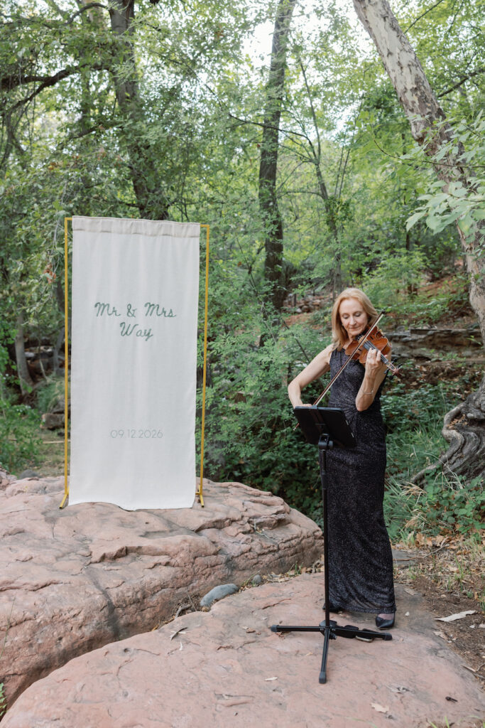 Live violinist playing beside the custom banner on the creek rocks