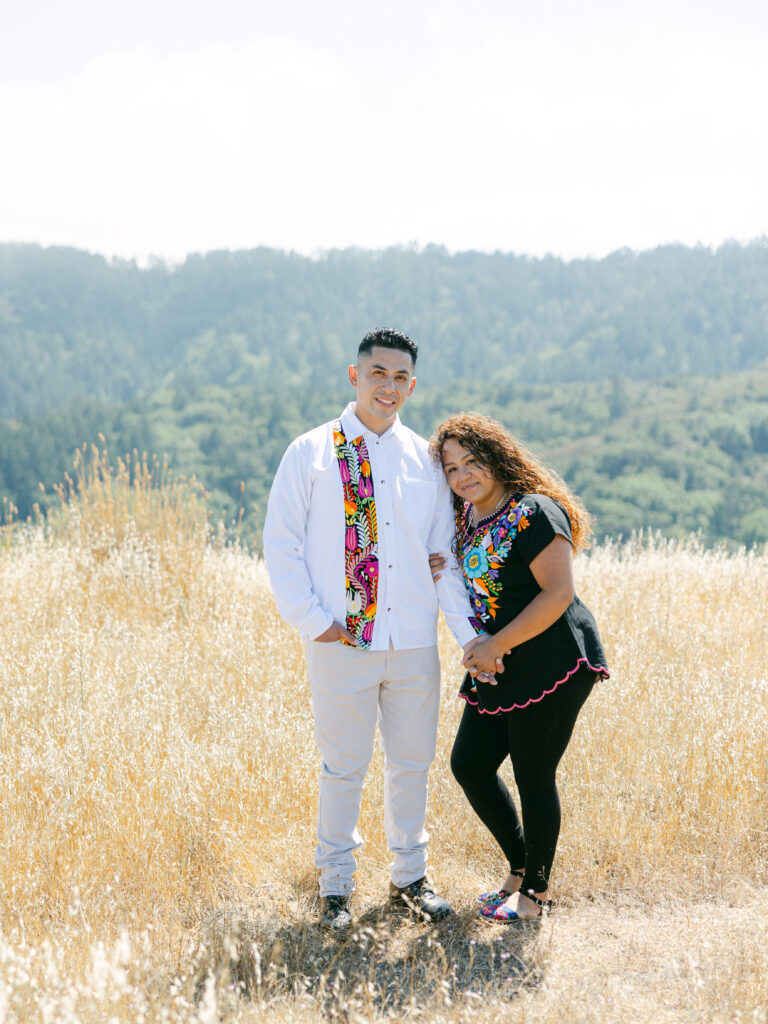 Engaged couple standing together in the golden hillside grass