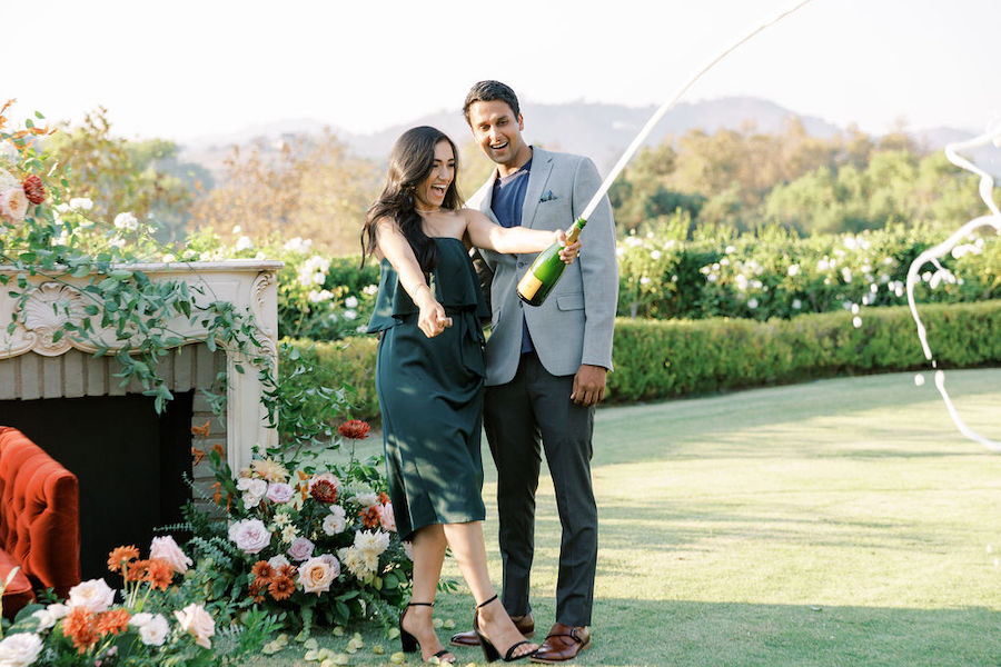 Man popping champagne beside his new fiancée
