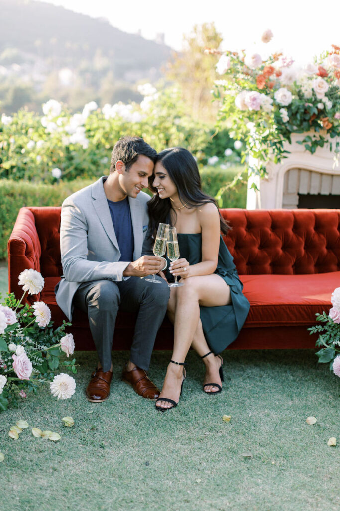 Couple sitting on a red velvet sofa with champagne in the garden