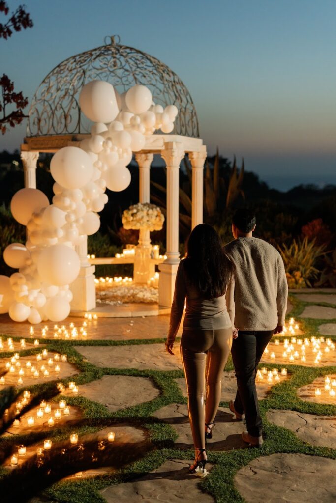 Couple walking toward a candlelit white gazebo at dusk for their Orange County proposal