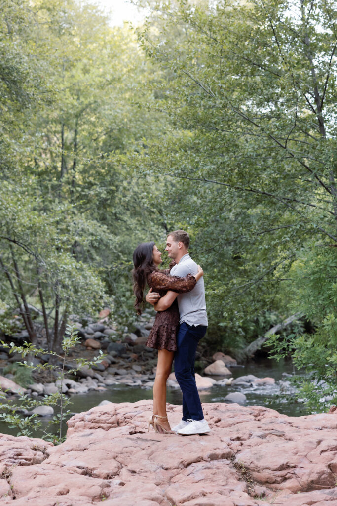Couple embracing on the red rocks at their Sedona creek proposal