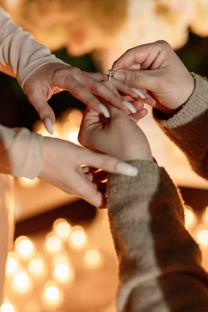 Close-up of him sliding the engagement ring onto her finger by candlelight