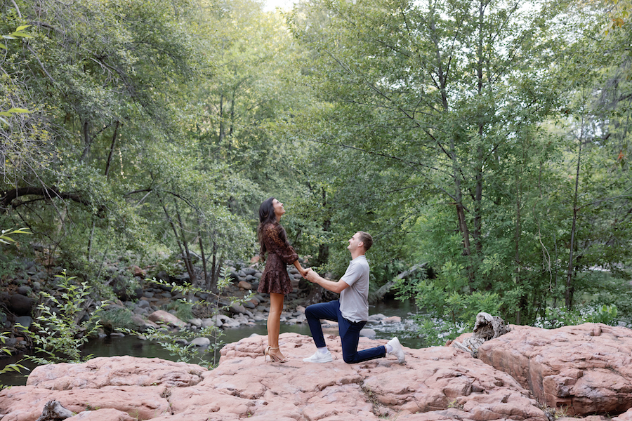 Beck on one knee on the red rock creek bed during their Sedona creek proposal