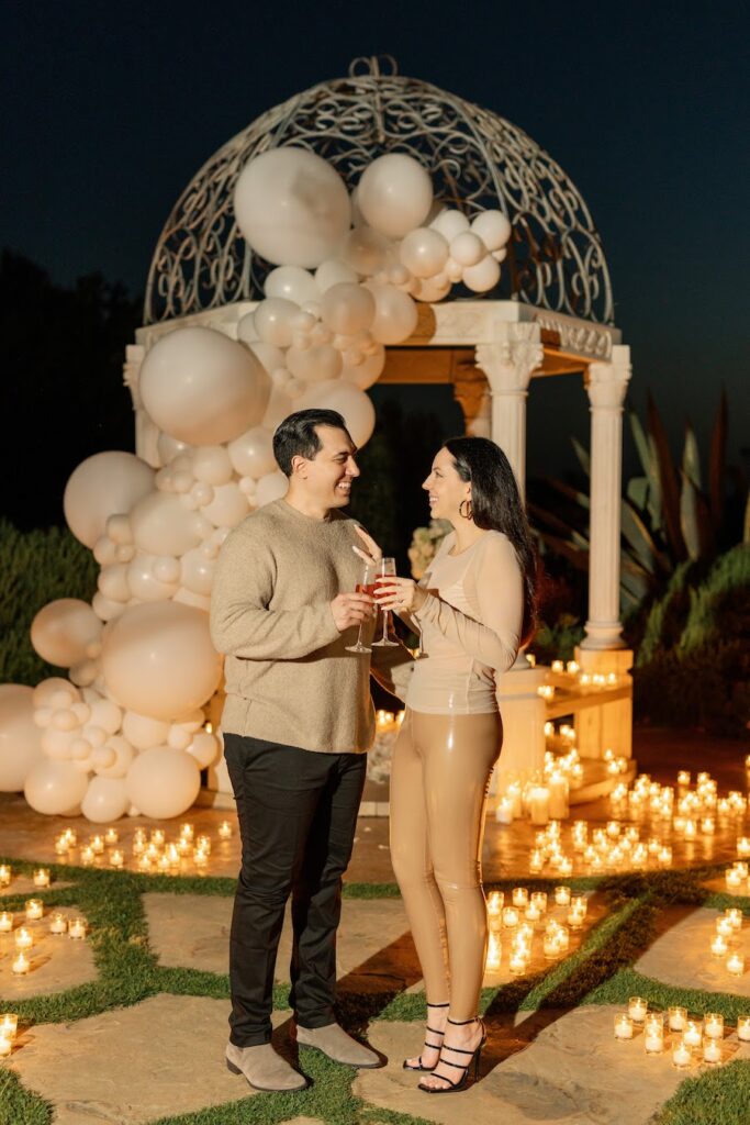 Engaged couple toasting champagne in front of the candlelit white gazebo