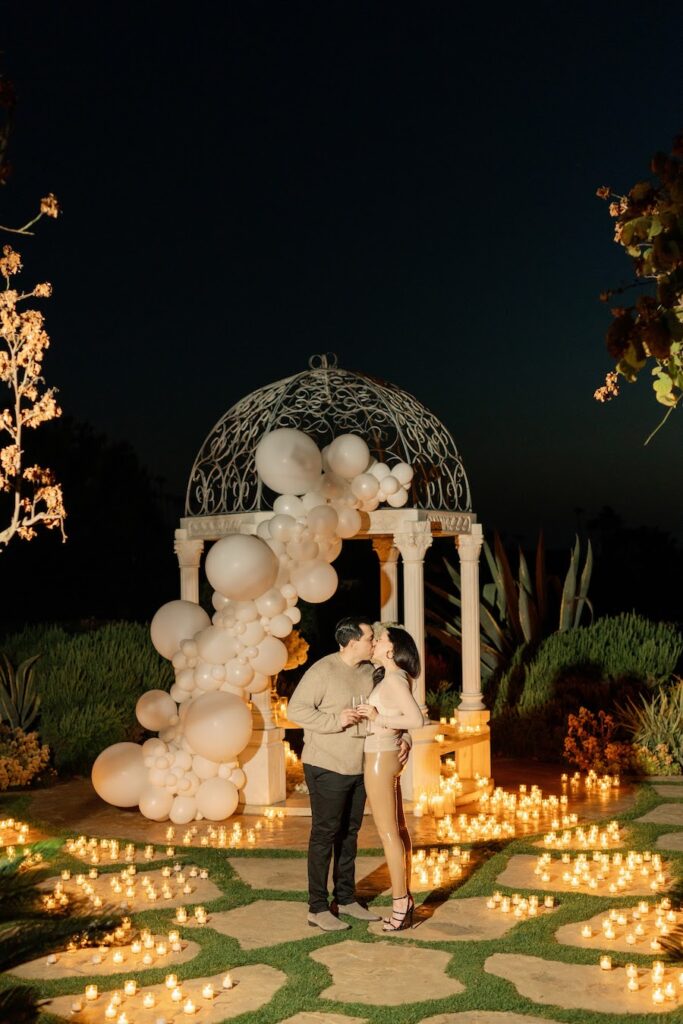 Newly engaged couple kissing beneath the white gazebo at night