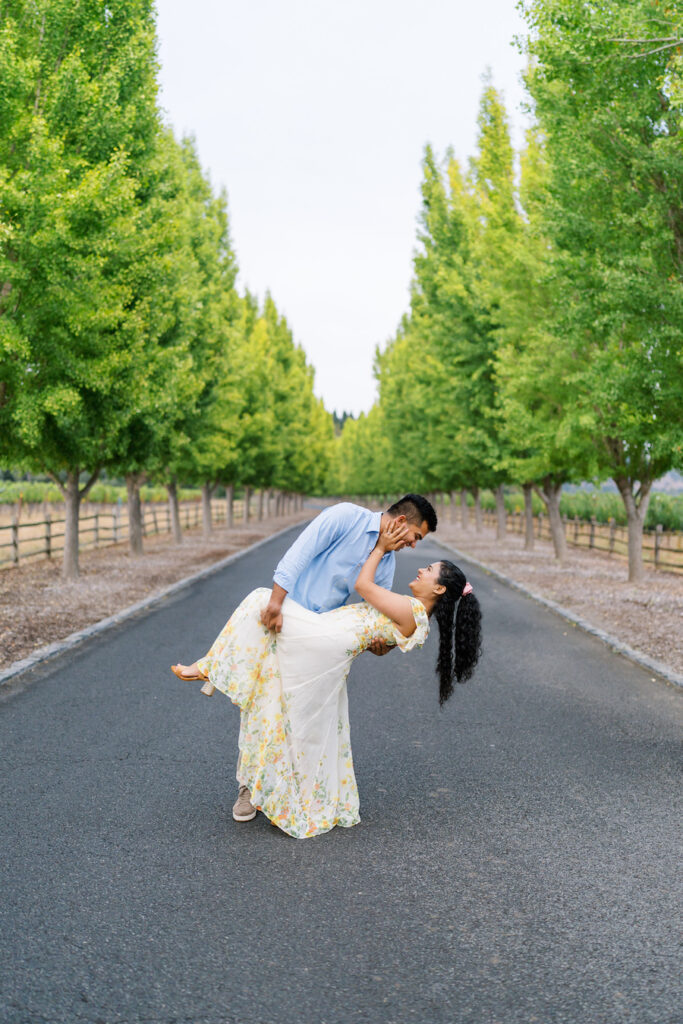 Man dipping her for a kiss on a tree-lined estate drive