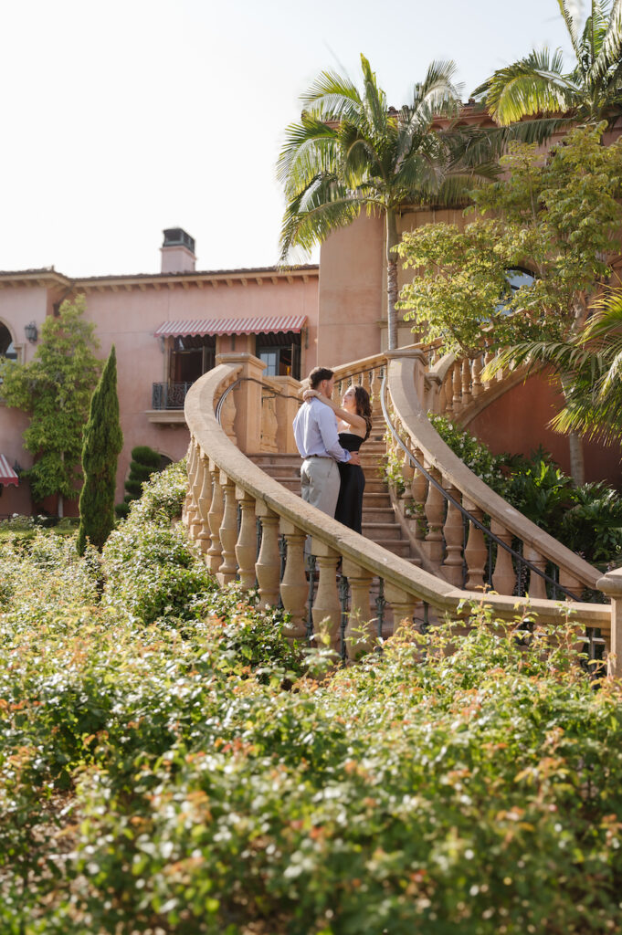 Engaged couple on a grand stone staircase surrounded by gardens