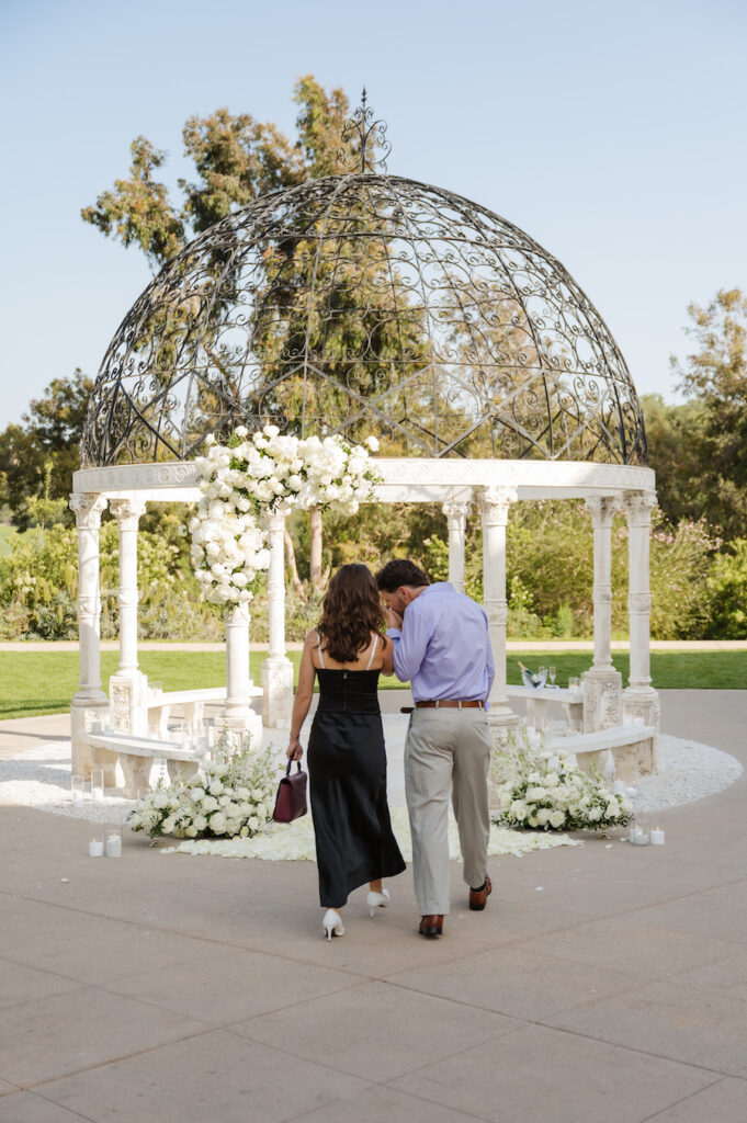 Couple walking toward the white floral gazebo for the proposal