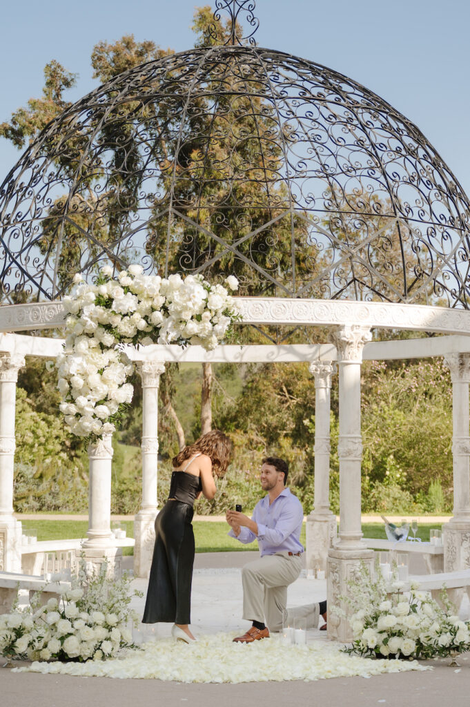Man on one knee proposing inside the all-white gazebo in San Diego
