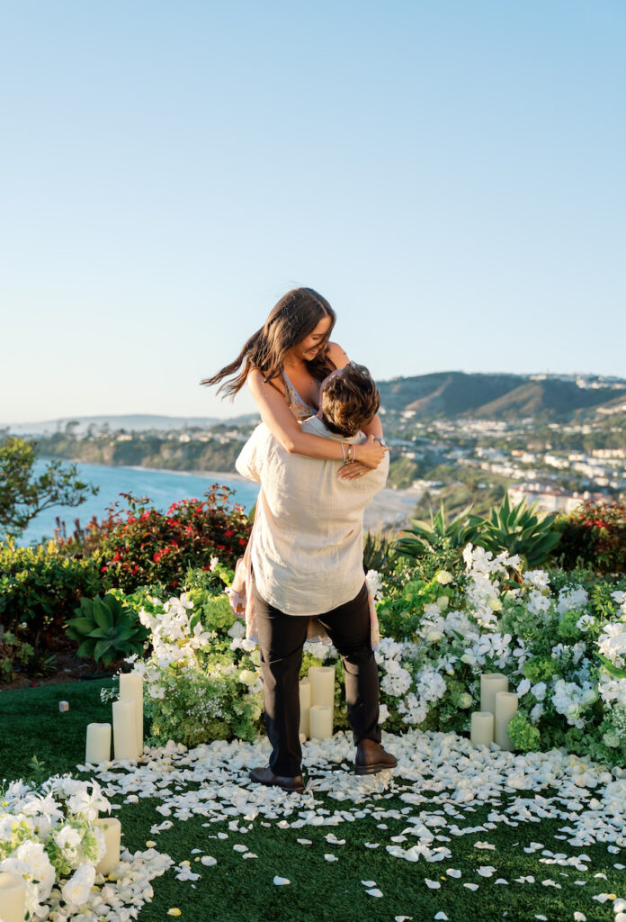 Cody lifting Nicole into a hug after the proposal with ocean views behind