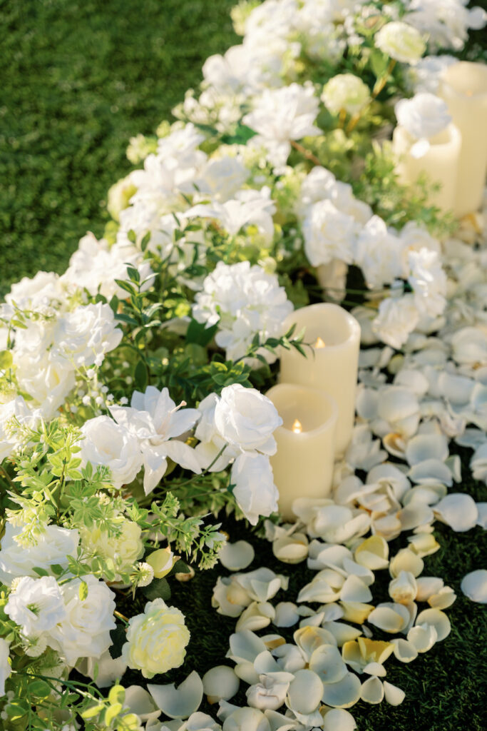 Close-up of white roses, gardenias and pillar candles along the petal aisle
