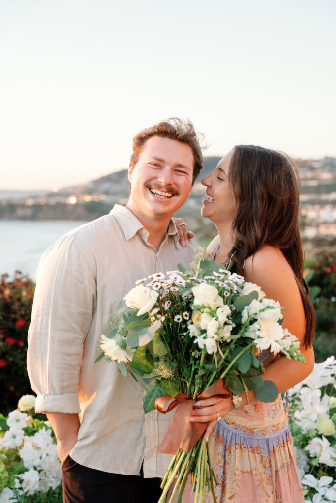 Cody and Nicole smiling with a white bouquet after their Ritz-Carlton proposal