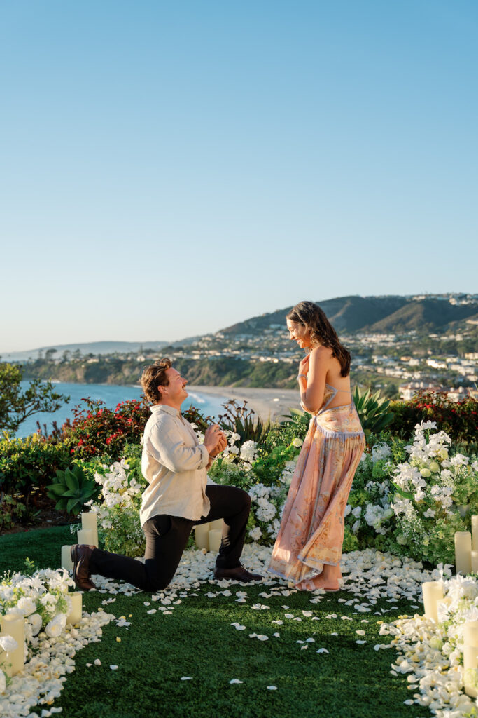 Cody on one knee during their Ritz-Carlton white floral proposal on the oceanfront lawn