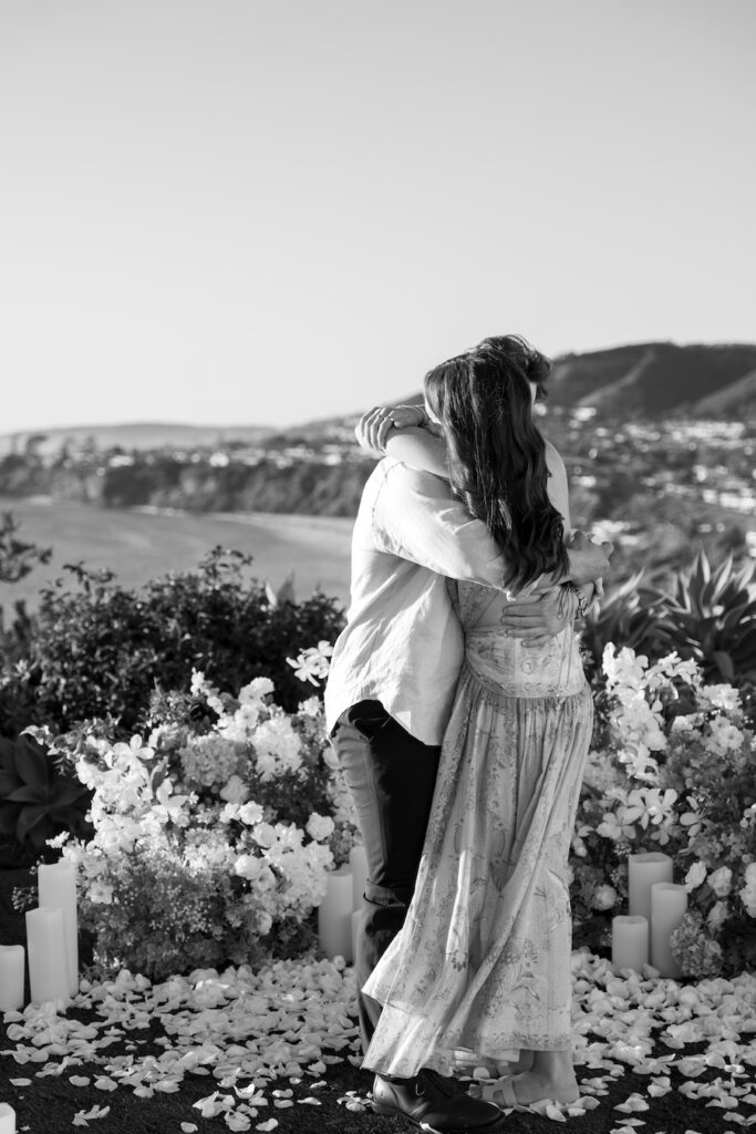 Black and white photo of the couple embracing among white florals and petals