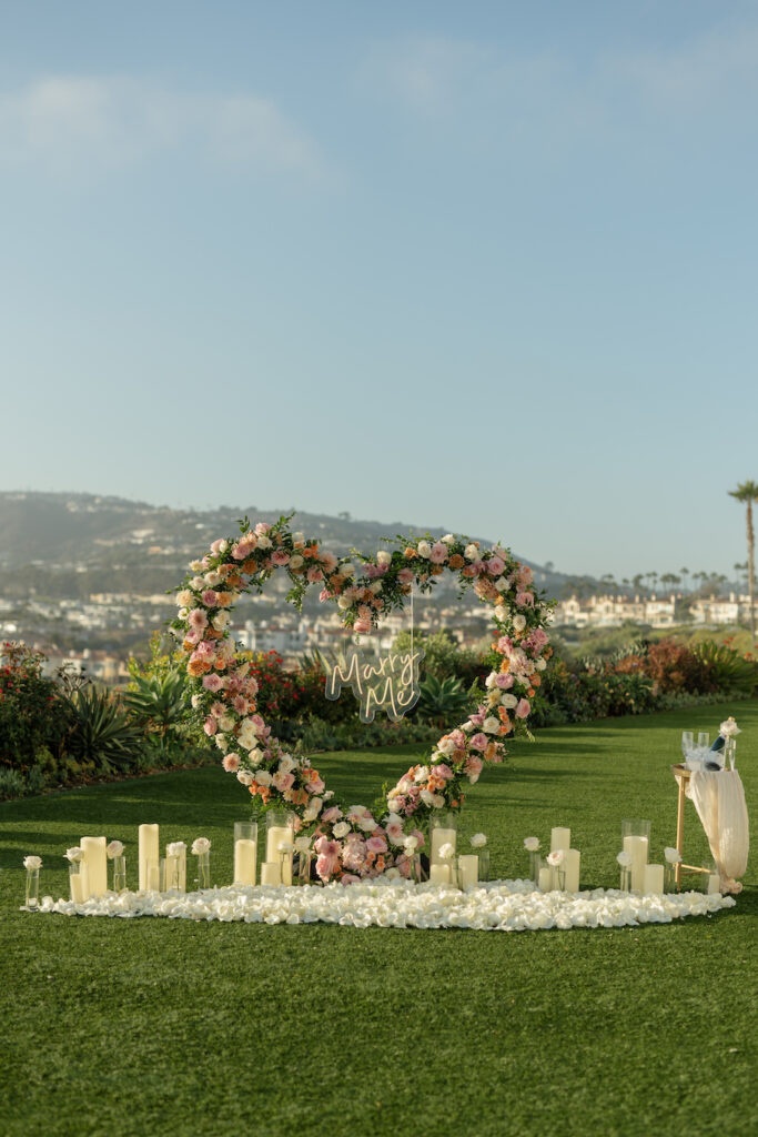 Ritz-Carlton heart arch proposal setup with blush and peach roses, candles and white petals overlooking the ocean