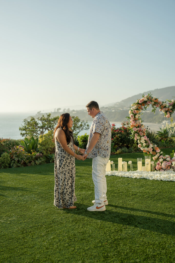 Couple holding hands in front of the Ritz-Carlton heart arch proposal at golden hour