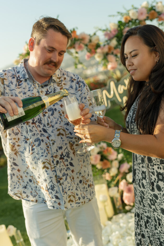 Champagne pour to celebrate the engagement beside the heart arch
