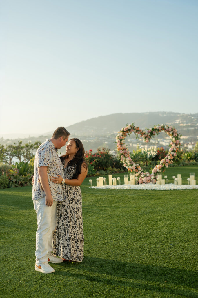 Newly engaged couple sharing a kiss in front of the heart arch with ocean views