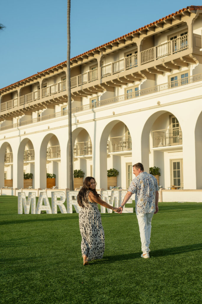 Couple walking hand in hand past the MARRY ME letters in front of the resort